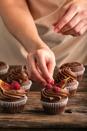 Close up photo of muffin preparation. vertical frame. Pastry chef decorates cupcakes with raspberries and figsの写真素材
