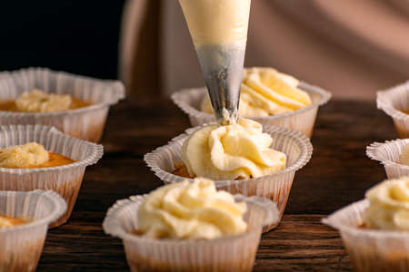 Baking cake in the kitchen vanilla muffin. Decorating cupcakes with cream from pastry bag. close upの写真素材