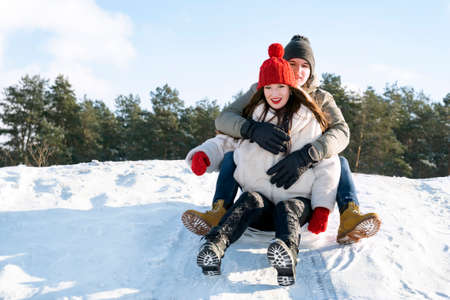 Young couple slide down the snow slide against the background of the forest and the blue sky. Winter...