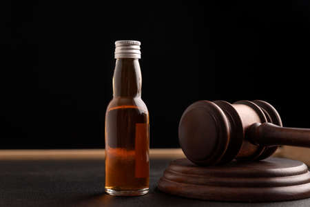 Judge gavel and bottle with whiskey or other alcohol on black background. alcohol and crime conceptの写真素材