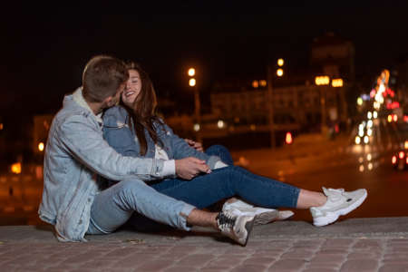 Young couple is sitting on the pavement embracing and hugging each other against the backdrop of the lights of the night city. copy spaceの写真素材