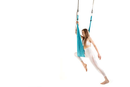 Girl trains on hammock on white background. Exercise of aerial gymnastics or fly yoga. Workout and stretching with sport hammockの写真素材