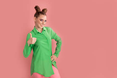 Young model in bright green blouse shows the gesture thumbs up. Portrait is girl with two funny buns...