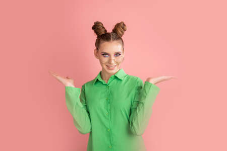 Girl in round glasses and with funny buns holds product or inscription on her palms. Space for your...