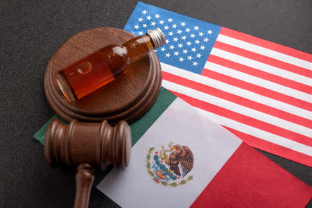 Bottle of whiskey or other alcohol and judge gavel on flags of the United States and Mexico. Alcohol policy. Illegal import of alcohol.の写真素材