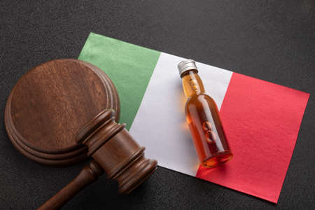 Lawsuit over alcohol in Italy. Bottle of alcohol and judge gavel on the flag of Italy. Alcohol and crime concept.の写真素材