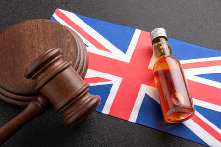 Bottle of alcohol and judge gavel on the flag of Great Britain. Alcohol law in UK. Alcohol and crimes in United Kingdom.の写真素材
