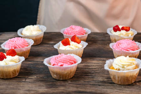 Cupcakes with cream and strawberries. Homemade vanilla muffins on wooden tableの写真素材