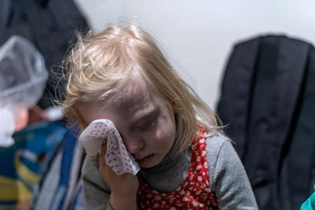 KHARKOV, UKRAINE- 3 MARCH 2022: little exhausted girl wipes face with handkerchief sitting in bomb shelter. Children hide in basementsのeditorial素材