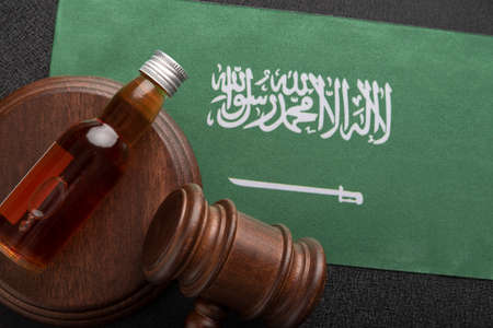 Bottle with whiskey or other alcohol and judge gavel on Flag of Saudi Arabia. alcohol and crime conceptの写真素材