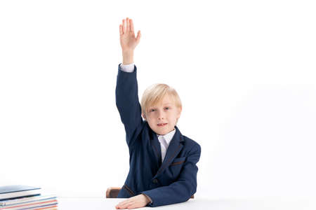 Seven-year-old boy in school uniform raised his hand high to answer the teachers question. Portrait...