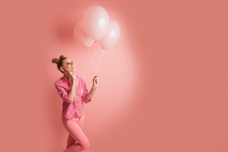 Cheerful happy girl in pink clothes and bun hairstyle holds inflatable balloons on pink background. copy spaceの写真素材