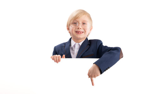 Boy in school uniform and large glasses with blank white poster board peeking. Schoolboy points his finger at something. copy spaceの写真素材