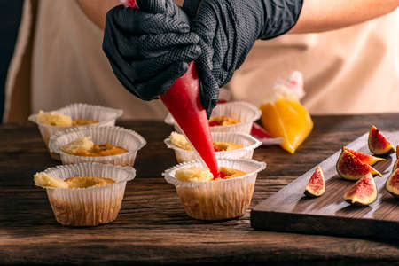 Pastry chef fills muffins with jam. Process of making cupcake by hand. Woman is cooking pastriesの写真素材