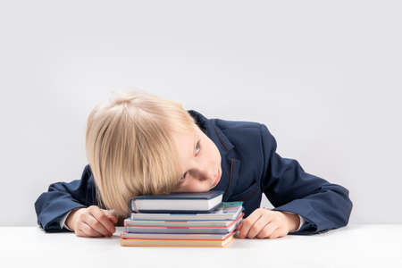 Upset schoolboy with pile of school books and notebooks. Tired or bored boy sleeps at the table