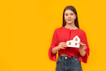 Girl holds toy house in her hands on yellow background. buy sell home. construction house. Rental Propertiesの写真素材