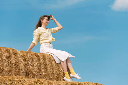 Pretty lady sits on straw and poses for photo. weekend in the countryside. summer dayの写真素材