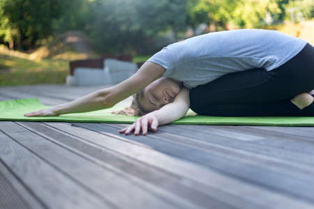 Young woman doing yoga exercises of stretching body in the green park. Practicing yoga outside at...