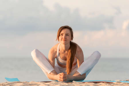 Young beautiful woman practicing yoga stretching outdoors by the sea. Yoga at sunrise on the beach