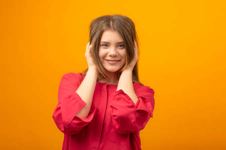 Young woman on yellow background. Portrait of attractive girl with hands behind head smiles and...