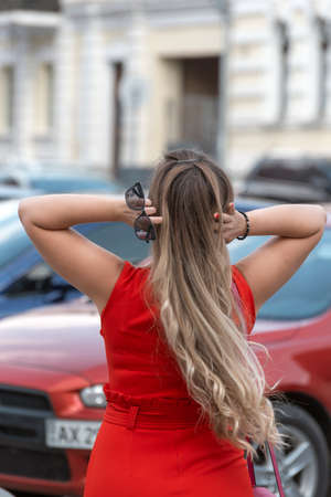 Blonde girl with long hair in red close fitting dress straighten hair. back view. vertical frameの写真素材