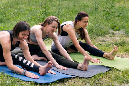 Young girls on yoga mats doing thigh muscle stretching exercises. Group fitness classes in nature.