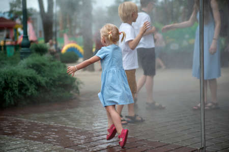 Children play under the water jets in summer park. Breeze on hot day. Walk in the park on a sunny day. playgroundの写真素材