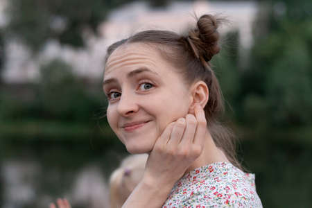 Portrait of cute young woman with two ponytails opened her eyes in surprise. Girl is holding on to her earの写真素材