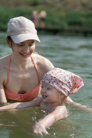 Happy mother with her little daughter swimming.Little girl splashes in the water and laughs. Summer holidays with childrenの写真素材