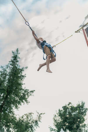 Little boy rides trampoline in an amusement park and jumps high into the sky. Child has fun in the theme parkの写真素材