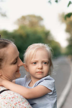 Young mother holds serious daughter in her arms and smiling sweetly. portrait of mother and blonde girlの写真素材