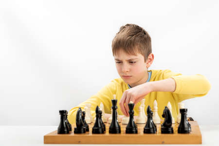 Boy plays chess and thinks intentionally about the next move. Portrait of teenager with chessboard isolated on white backgroundの写真素材