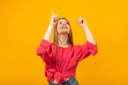 Attractive girl looks up in surprise and points her fingers at something. young woman pointing to...