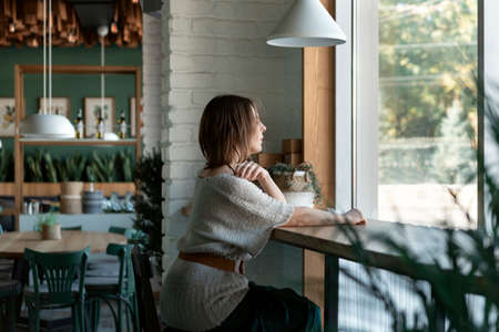 Young woman sitting alone in cafe near window. Attractive woman relaxes in cafe inside