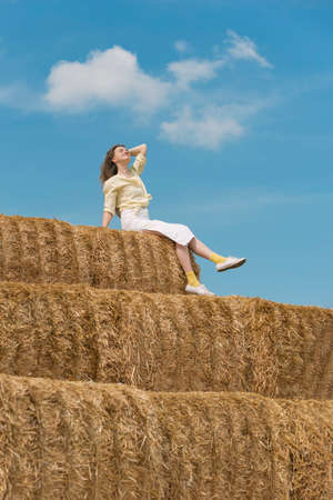 Lovely young woman sits on huge haystack. local tourism. Sunny day at the farm. country side holidayの写真素材