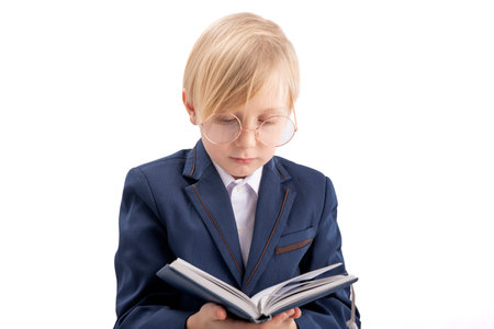Blond boy in school uniform reads textbook. Schoolboy with big glasses looks at book. isolated on...
