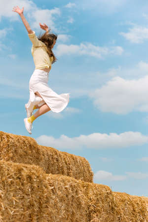 Woman while jumping on big haystack. Girl has fun and jumps in the hay on blue background. summer holidays.の写真素材