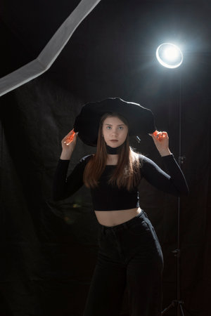 Portrait of young woman in stylish black clothes and hat with wide brims. Young girl in gothic style. Black background. vertical frameの写真素材