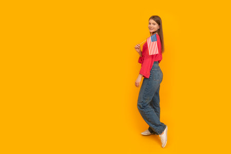 Young girl with an American flag in her hands. Full-length portrait of teenager on yellow background. copy spaceの写真素材