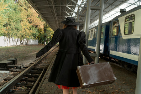 Woman in black coat and hat with retro suitcase rushes to train. back view. Photo in vintage retro...