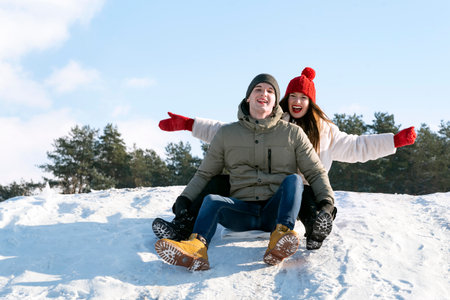 Young couple slide down the snow slide. Winter sunny day. Man and woman gainst the background of the forest and the blue skyの写真素材