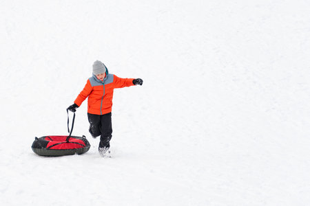 Boy runs through snow drags inflatable sled. Young child on snow background in winter.の写真素材