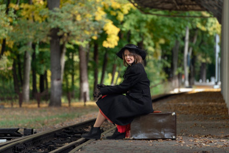 Middle-aged woman with retro suitcase at the train station waiting for train. Style 30-40s. Vintage clothes in autumn on platform.の写真素材