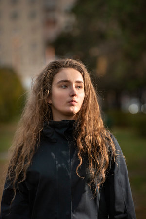 Portrait of pretty pensive girl with long wavy hair. Photo of young woman in autumn park.