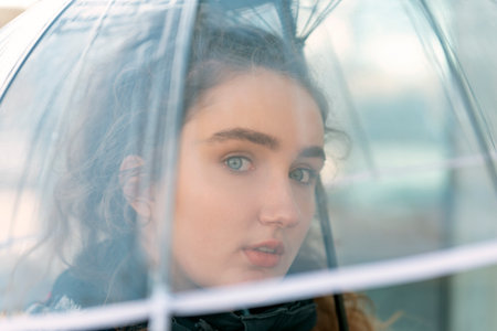 Young beautiful woman with blue eyes with transparent umbrella and look thoughtfully straight....