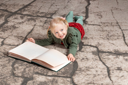 Two-year-old girl lies on floor and flips through book with blank empty pages. copyspace. Christmas Eve.の写真素材