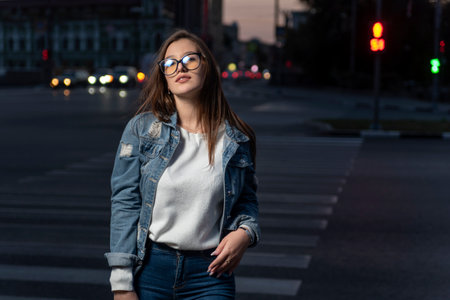 Portrait of brunette girl in youth clothes on evening city background. Stylish young woman in glasses on city street, summer timeの写真素材