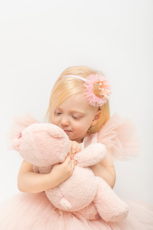 Pretty little girl hugs pink teddy bear. Blonde girl in lush pink dress and hoop decoration. white background. vertical frame.の写真素材