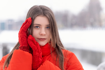 Close up portrait of blue-eyed eyes girl in red warm jacket and mittens in winter outside. Youth warm clothing.の写真素材