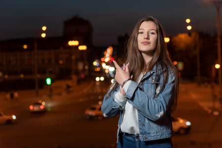 Happy girl student walks around the evening city. Young brunette woman in denim clothes on evening city backgroundの写真素材